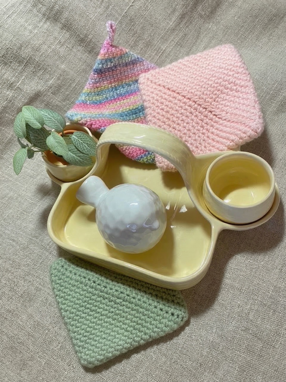 Crocheted soup bowl cozies in pink, mint green, and rainbow stripe displayed with a yellow ceramic tea tray